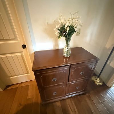 Vintage four-drawer wooden filing cabinet with a dark brown finish and recessed panel drawer fronts, topped with a decorative floral...