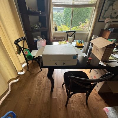 Dark wood dining table with curved legs, paired with matching cross-back chairs, shown with various storage boxes and household items.