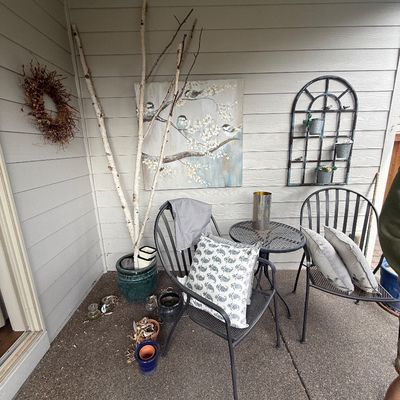 Three-piece black metal patio bistro set with two chairs and a small round table, shown with outdoor decor including a bird canvas print...