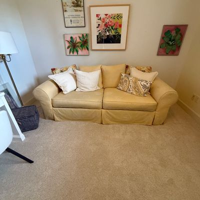 Yellow rolled-arm sofa with a skirted base, styled with assorted throw pillows, positioned beneath a gallery wall of framed floral and...