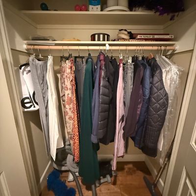 Assorted women's clothing, including jackets, pants, and dresses, hanging in a closet alongside board games and household items.