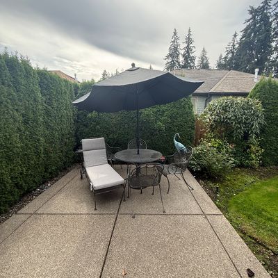 Wrought iron patio dining set including a round mesh table, three matching chairs, a large black umbrella, and a coordinating chaise...