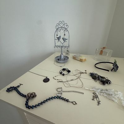 Assorted costume jewelry, including beaded necklaces, chains, and bracelets, displayed on a white dresser alongside a small wire jewelry...