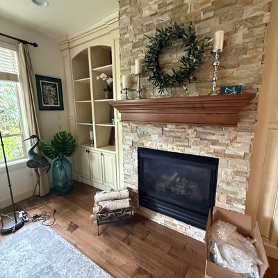 Living room fireplace area featuring a stone veneer surround, a wooden mantel decorated with a wreath and candlesticks, a metal log...
