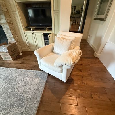 Contemporary cream-colored upholstered armchair with matching throw pillows, positioned on a hardwood floor.