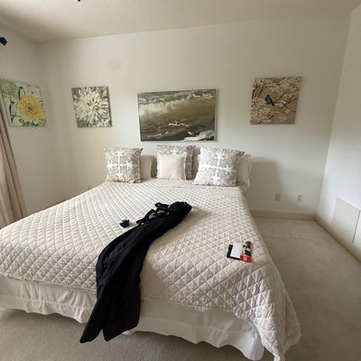 Bed with a white quilted coverlet, matching patterned throw pillows, and a selection of framed wall art hanging above.