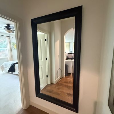 Large rectangular wall mirror featuring a thick, dark brown or black wooden frame, mounted in a hallway.
