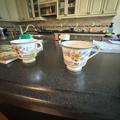 Pair of vintage porcelain teacups featuring a delicate floral pattern with gold trim, displayed on a dark kitchen countertop.