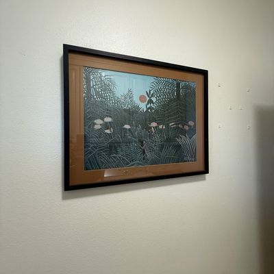 Framed print of Henri Rousseau's "The Equatorial Jungle," featuring a lush jungle scene with a red sun, housed in a black...