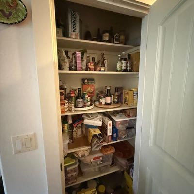 A kitchen pantry closet with multiple shelves stocked with various canned goods, boxed foods, condiments, and storage containers.