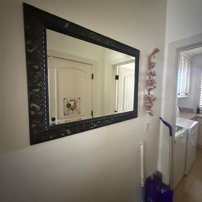Large rectangular wall mirror featuring a dark, textured frame with carved details, mounted in a hallway.