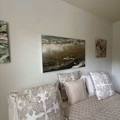 Contemporary bedroom decor featuring a neutral-toned quilted coverlet, patterned throw pillows, and framed abstract landscape wall art.