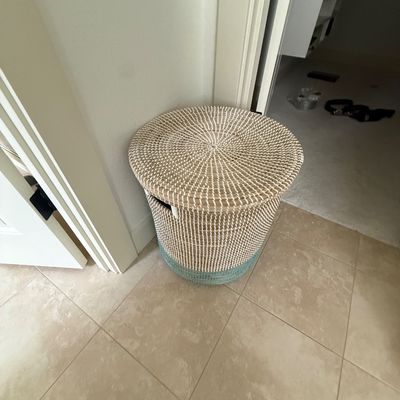 Woven seagrass laundry hamper with a matching lid, featuring a natural and white pattern with a light blue accent band at the base.