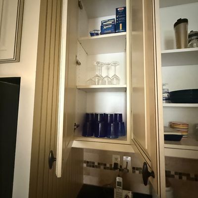 Open kitchen cabinets displaying a selection of glassware, including wine glasses and blue tumblers, alongside pantry items.