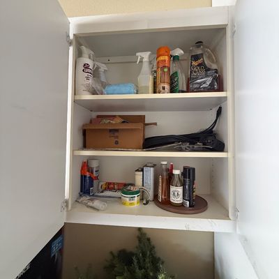 White wall cabinet containing various household cleaning supplies, car wash soap, extension cords, and small tools.