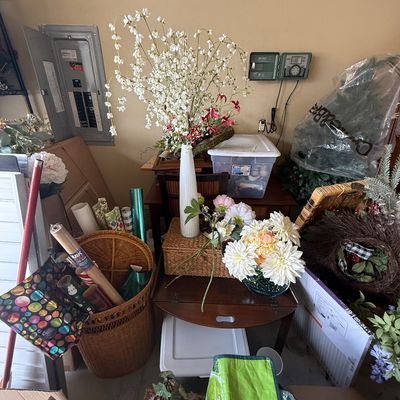 Assorted home decor and holiday items, including artificial floral arrangements, a wicker basket filled with wrapping paper, and various...