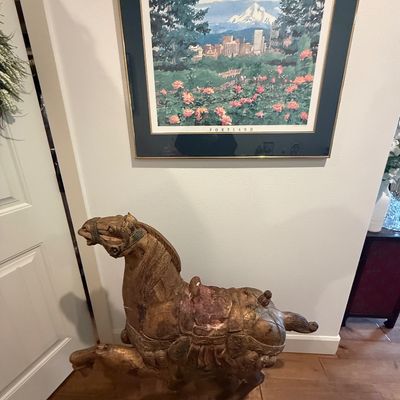 Vintage carved wooden Tang-style horse sculpture with a distressed gold finish, displayed beneath a framed Portland, Oregon art print.