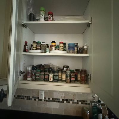 Assorted kitchen spices, seasonings, and condiments organized on the shelves of a white cabinet.