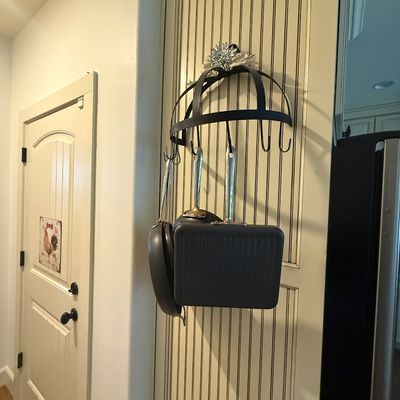 Wall-mounted black metal pot rack with hooks, holding a selection of modern non-stick cookware including a square grill pan and skillets.
