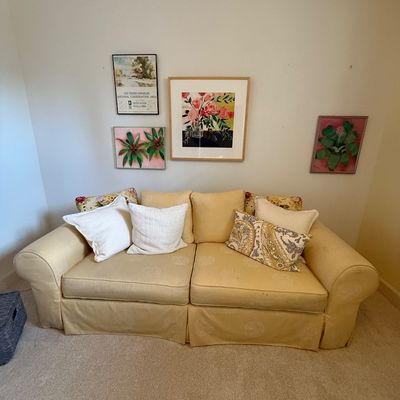 Traditional rolled-arm sofa in a pale yellow damask fabric, styled with assorted throw pillows, positioned beneath a gallery wall of...