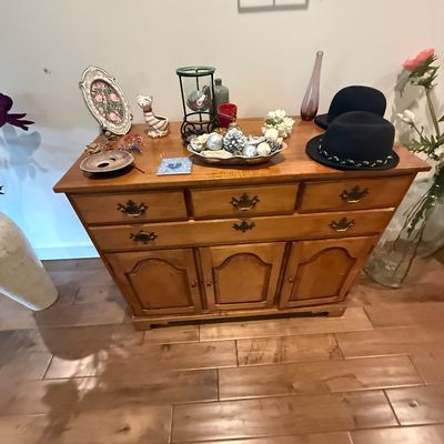 Vintage maple buffet featuring three upper drawers with brass batwing pulls and three lower cabinet doors, styled with various decorative...