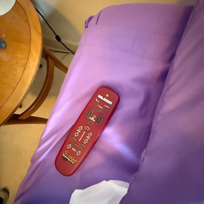 Wallhugger S-Cape adjustable bed remote control in red, resting on a purple-sheeted bed.