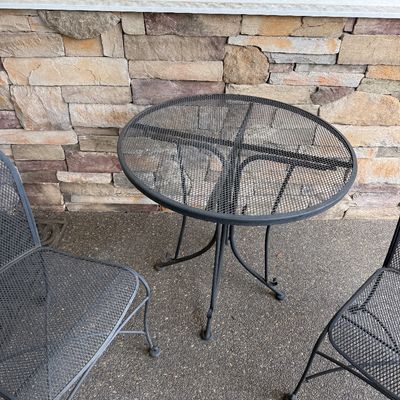 Vintage black wrought iron patio set including a round mesh-top bistro table and two matching mesh chairs.
