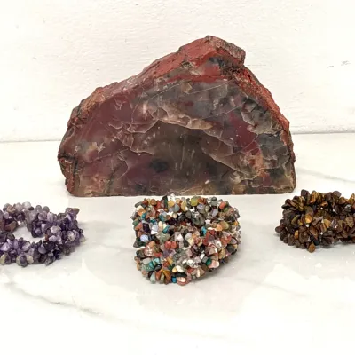 Sale Photo Thumbnail #410: Polished petrified wood slab specimen displayed alongside three natural gemstone chip stretch bracelets, including amethyst, mixed jasper, and tiger's eye.