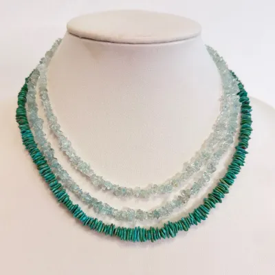 Sale Photo Thumbnail #169: Three-strand gemstone necklace featuring two inner strands of light blue aquamarine chip beads and an outer strand of turquoise disc beads, displayed on a white jewelry bust.