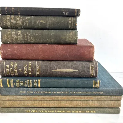 Sale Photo Thumbnail #204: Stack of vintage medical books and textbooks, including volumes from The Ciba Collection of Medical Illustrations by Netter, Saunders, and Mosby, showing aged cloth covers and gilt lettering.