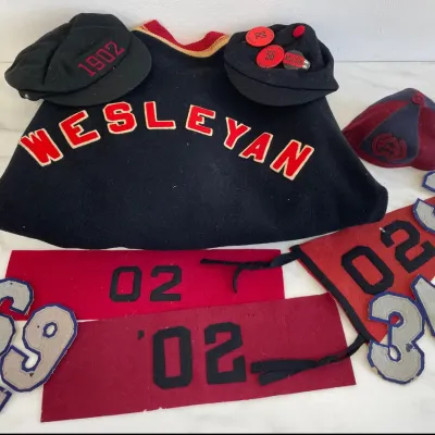 Sale Photo Thumbnail #119: Collection of vintage Wesleyan University memorabilia, including a black wool letterman sweater, felt class year banners from '02, collegiate caps, and assorted felt varsity numbers.