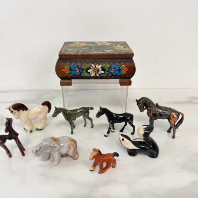 Sale Photo Thumbnail #78: Collection of vintage miniature animal figurines, including ceramic and metal horses, a skunk, and an elephant, displayed alongside a hand-painted wooden trinket box.