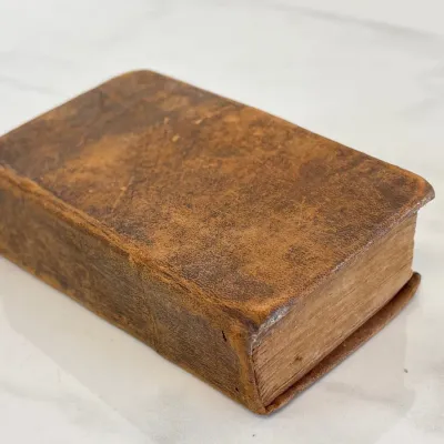 Sale Photo Thumbnail #207: Antique miniature leather-bound book featuring a heavily distressed brown calfskin cover and aged, yellowed pages.