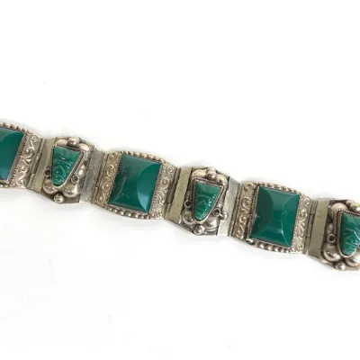 Sale Photo Thumbnail #173: Vintage Mexican sterling silver link bracelet featuring alternating panels of bezel-set green onyx and carved green onyx mask cabochons, showcasing detailed beadwork and scroll engraving.