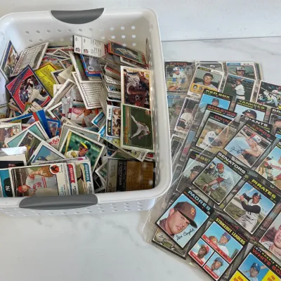 Sale Photo Thumbnail #123: Large collection of vintage Topps baseball cards from the 1970s and 1980s, featuring a loose assortment in a white plastic basket alongside several cards in protective plastic binder sleeves.
