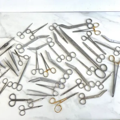 Sale Photo Thumbnail #122: Large collection of vintage stainless steel medical instruments, including surgical scissors, forceps, clamps, and tweezers, displayed on a marble surface.