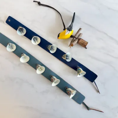 Sale Photo Thumbnail #157: Two vintage leather strap door hangers featuring five metal bells each, alongside a hand-painted wooden yellow bird ornament perched on twigs.