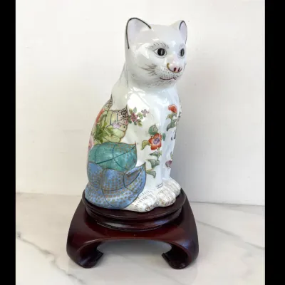 Sale Photo Thumbnail #44: Vintage Chinese Famille Rose porcelain cat figurine, hand-painted with floral and leaf motifs, displayed on a custom carved wooden stand.