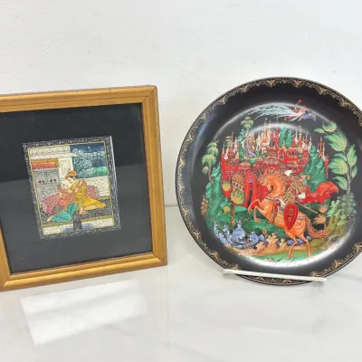 Sale Photo Thumbnail #259: Persian miniature painting depicting a courtly scene in a gold frame, shown alongside a Russian lacquer collector plate featuring a traditional folklore illustration.