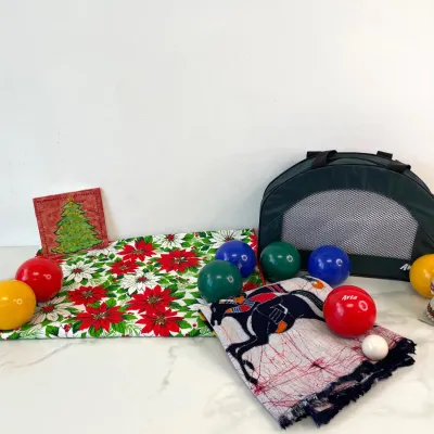 Sale Photo Thumbnail #71: Avta bocce ball set with carrying case, featuring colorful balls and a small white pallino, displayed alongside a festive poinsettia table runner, a Christmas tree trivet, a patterned scarf, and a small decorative doll.