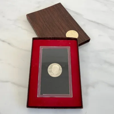 Sale Photo Thumbnail #238: A 1971 United States Eisenhower uncirculated silver dollar coin, housed in its original US Mint presentation case with a red velvet insert and wood-grain slipcase.