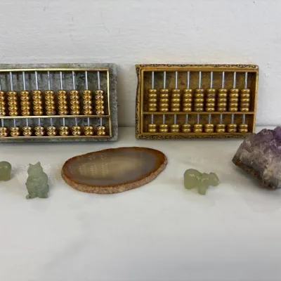 Sale Photo Thumbnail #45: Two miniature brass abacuses, one with a jade base, displayed alongside three small carved jade animal figurines, an agate slice, and an amethyst crystal cluster.