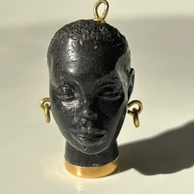 Sale Photo Thumbnail #270: Vintage black resin African woman bust pendant, featuring gold-tone hoop earrings, a matching gold-tone collar base, and a top bail loop for necklace attachment.