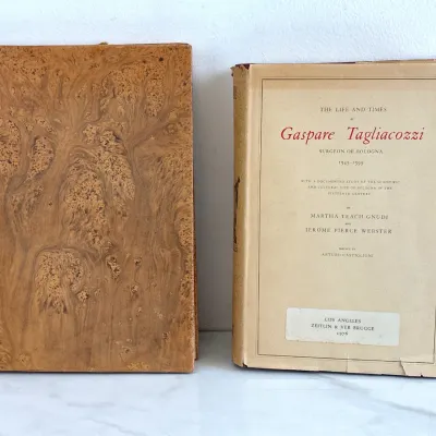 Sale Photo Thumbnail #195: Two vintage books on history and medicine, including a 1976 edition of "The Life and Times of Gaspare Tagliacozzi" published by Zeitlin & Ver Brugge, alongside a marbled-cover antiquarian volume.