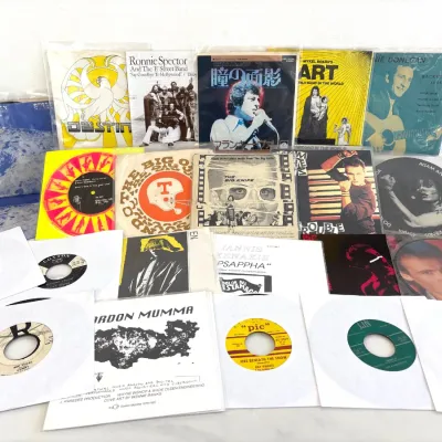 Sale Photo Thumbnail #285: Collection of vintage 7-inch vinyl records and 45 RPM singles, featuring artists like Ronnie Spector, Gordon Mumma, and Adam and the Ants, complete with original picture sleeves and paper covers.