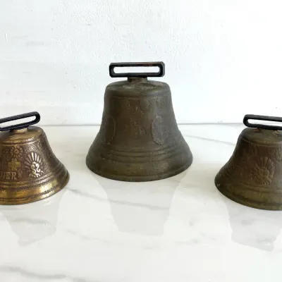 Sale Photo Thumbnail #146: Trio of vintage Swiss bronze cowbells, featuring embossed floral and cross motifs with integrated strap loops.