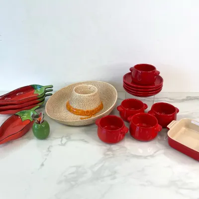 Sale Photo Thumbnail #65: Le Creuset red stoneware baking dish and matching soup bowls with saucers, paired with a festive Mexican-themed serving set including chili pepper plates and a ceramic sombrero chip and dip platter.