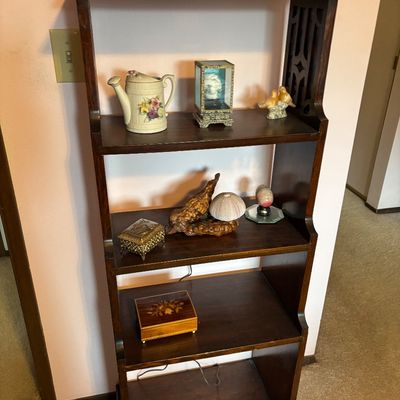 Vintage dark wood five-tier bookshelf with decorative fretwork on the upper sides, displaying various small collectibles and trinket boxes.