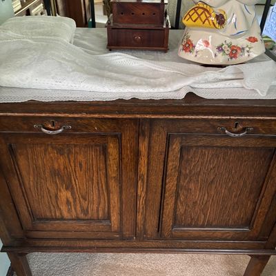 Vintage oak cabinet with two paneled doors, displaying a white lace runner, a small wooden box with a drawer, and a ceramic Little Red...