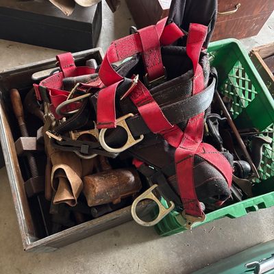 Heavy-duty safety harness with red and black webbing and metal D-rings, resting on crates filled with vintage hand tools.